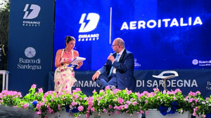 Intervista sul palco durante un evento Dinamo Basket e Aeroitalia, con i loghi dei partner sullo sfondo.