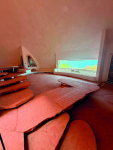 Interno della cupola con arredi in pietra e grande finestra panoramica affacciata sul mare.