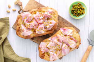Pinsa farcita con mortadella e granella di pistacchio servita su un tagliere di legno.