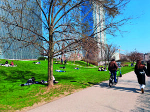 Parco pubblico a Milano con persone sul prato, pista ciclopedonale e grattacieli moderni sullo sfondo.