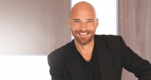 Andrea Pezzi, dal teatro all’IA: “Per una nuova intelligenza naturale”. Ritratto di Andrea Pezzi sorridente, seduto con giacca nera in un ambiente moderno.