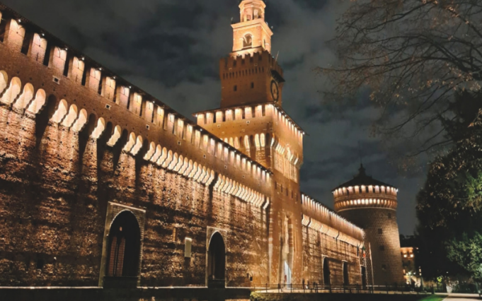Castello Sforzesco di Milano illuminato di notte, con la Torre del Filarete e le mura in mattoni.