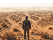 La forza della fragilità Viaggiatore con zaino osserva un paesaggio desertico attraversato da numerose piste sterrate.