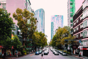 Strada urbana di Citt&agrave; del Messico con traffico, alberi e moderni grattacieli sullo sfondo.