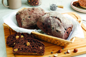 Pane al cacao con nocciole intere, servito a fette su un tagliere di legno.