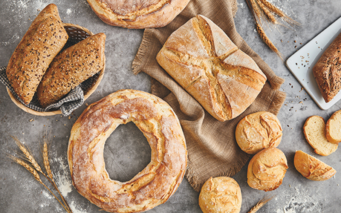 pane surgelato Assortimento di pani artigianali di diverse forme e tipi, con spighe di grano su un piano infarinato.